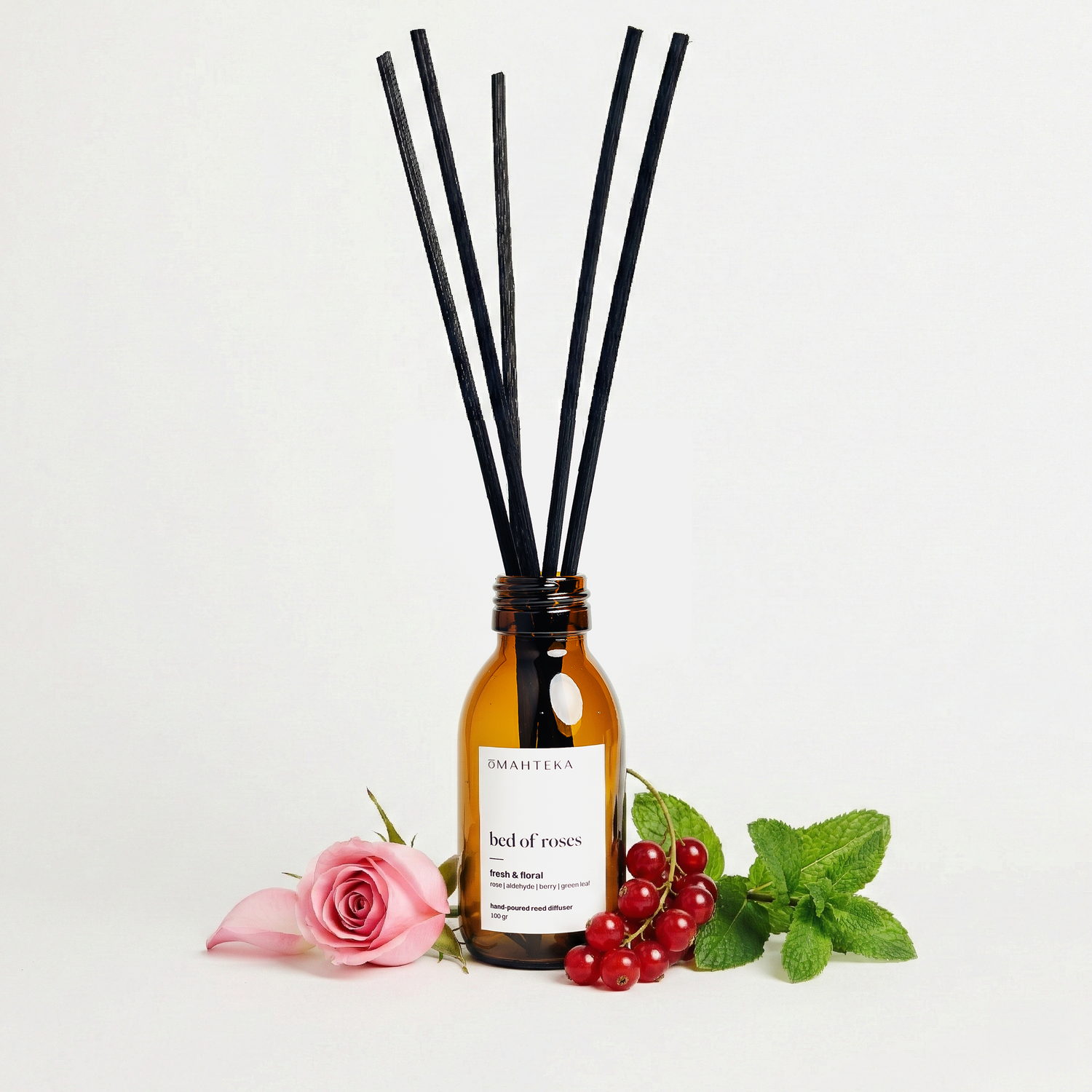 Bed of Roses de la Omahteka – parfum de cameră cu bețișoare, într-un cadru cu frunze picurate de rouă, plante verzi și petale de trandafiri.