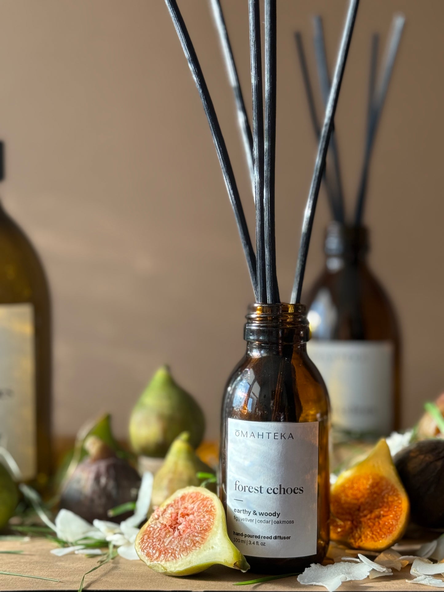Parfum de cameră Forest Echoes de la Omahteka – difuzor cu bețișoare din ratan și sticlă maro cu protecție UV, în decor natural cu smochine și lemn.