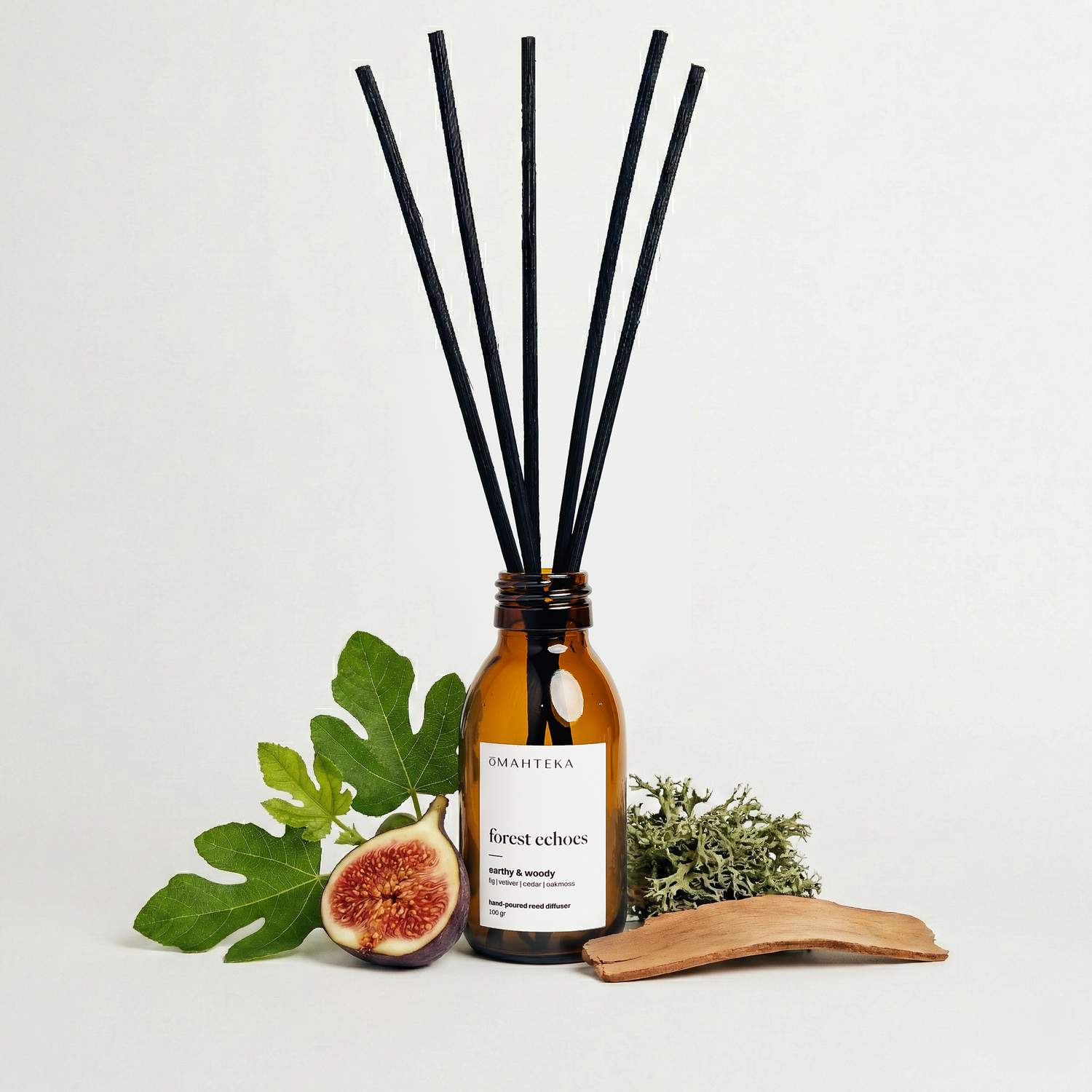 Parfum de cameră Omahteka Forest Echoes, înconjurat de iarbă verde și bucăți de lemn – o esență inspirată din natură, ideală pentru relaxare.