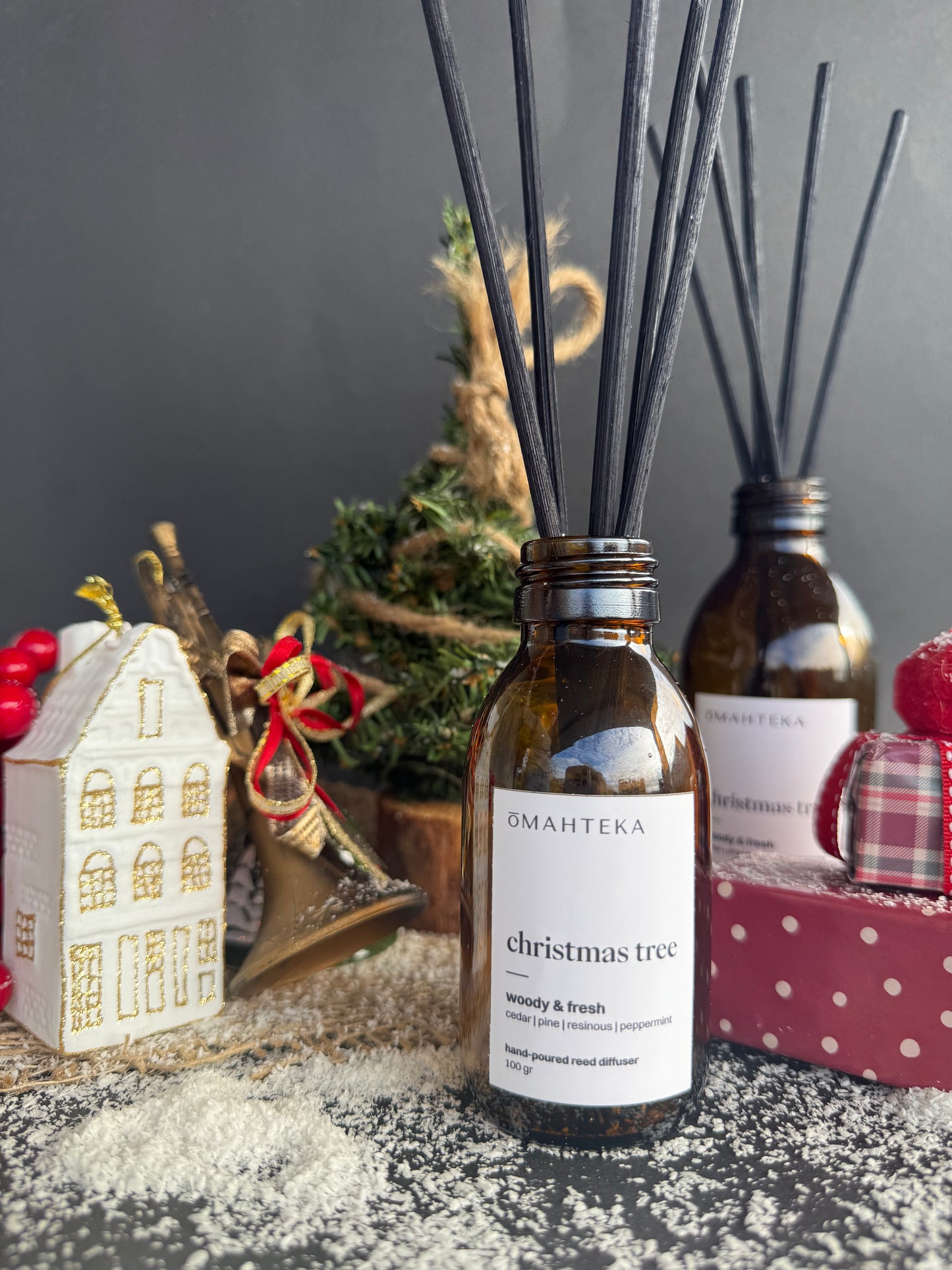 Parfum de cameră Christmas Tree cu betisoare negre, înconjurat de decoruri inspirate din pădurea de iarnă.