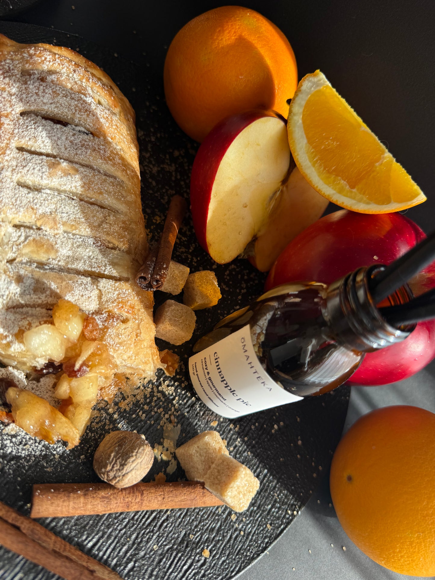 Sticla Cinnapple Pie cu protecție UV, decorată cu ingrediente ce reflectă notele parfumului: măr, scorțișoară și zahăr brun.