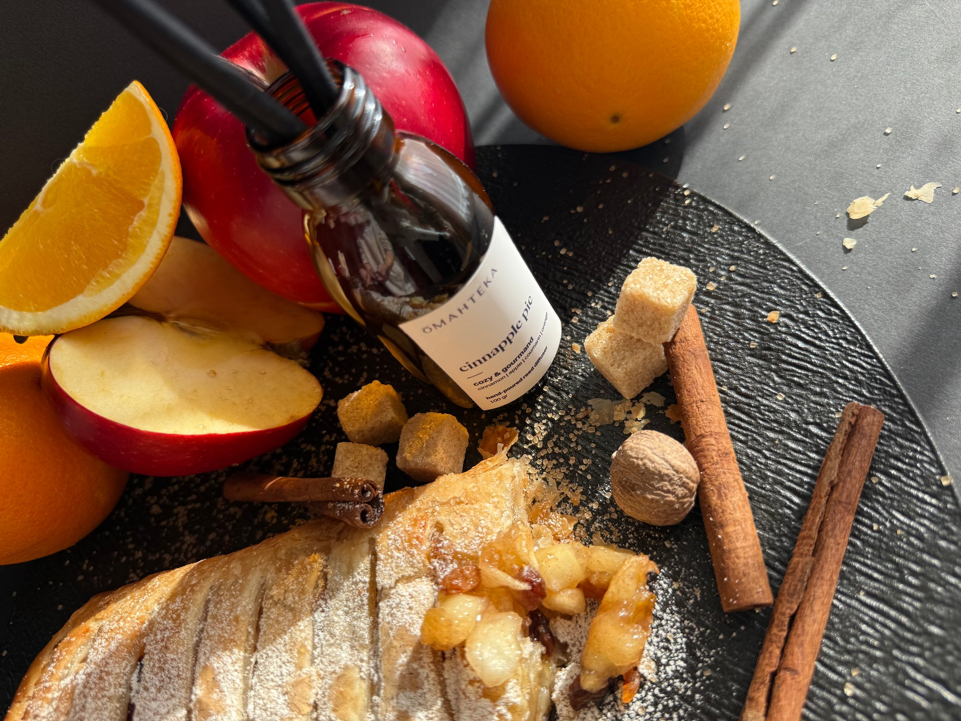 Omahteka Cinnapple Pie, într-un cadru gurmand cu felii de portocală, mere și condimente dulci.