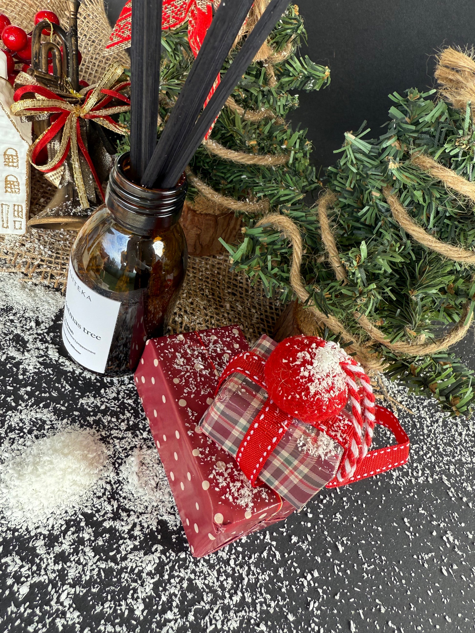 Difuzorul de cameră într-o scenă festivă cu globuri, ramuri de brad și elemente lemnoase ce reflectă notele parfumului.