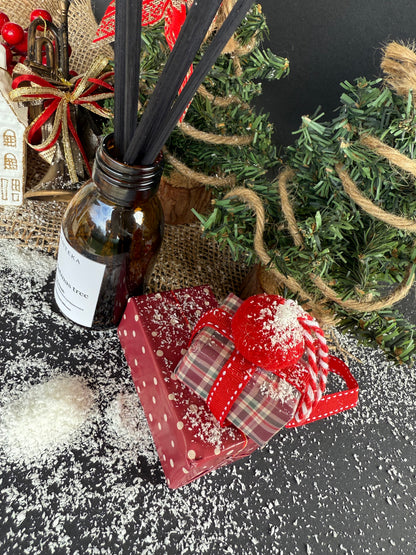 Difuzorul de cameră într-o scenă festivă cu globuri, ramuri de brad și elemente lemnoase ce reflectă notele parfumului.