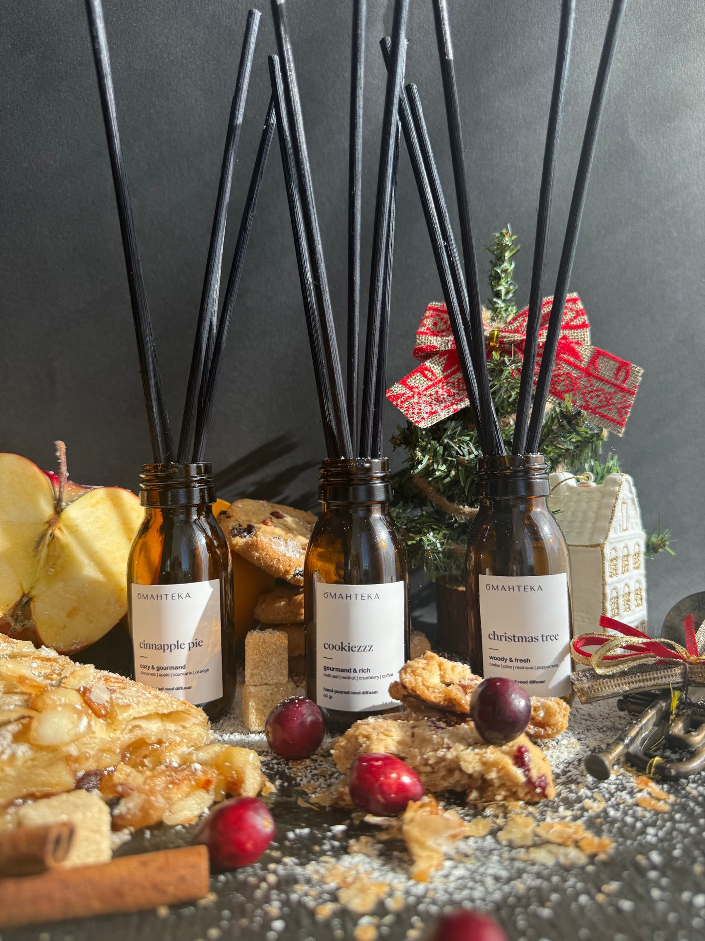 Setul Christmas Discovery Omahteka cu cele trei parfumuri de cameră, prezentate într-un decor festiv cu globuri și brad.