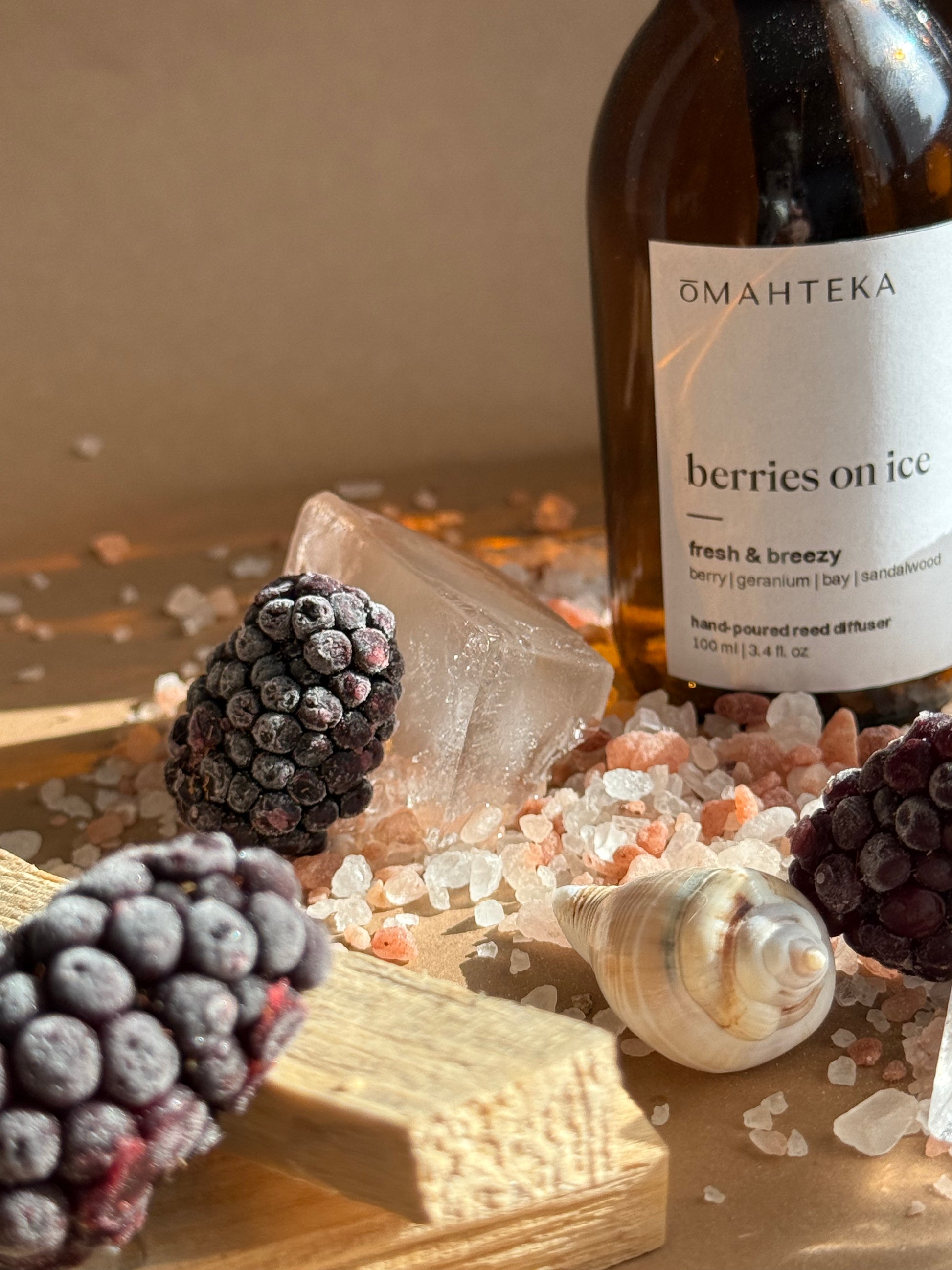 Sticla cu parfum de cameră Berries on Ice în sticlă maro și bețișoare din ratan, în decor minimalist cu accente marine și fructate.

