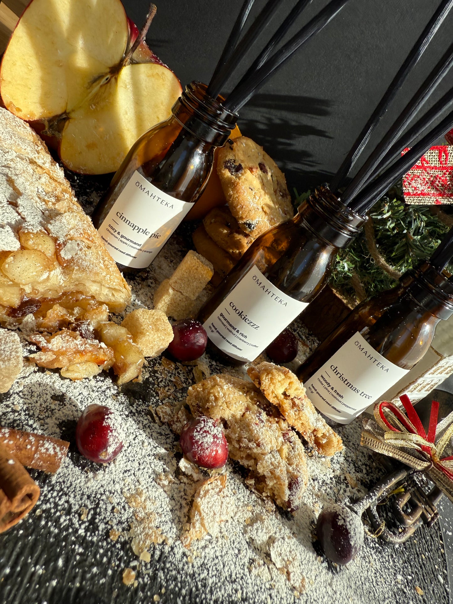 Parfumurile de cameră cu betișoare negre, înconjurate de elemente de iarnă: brad, globuri și texturi cozy.