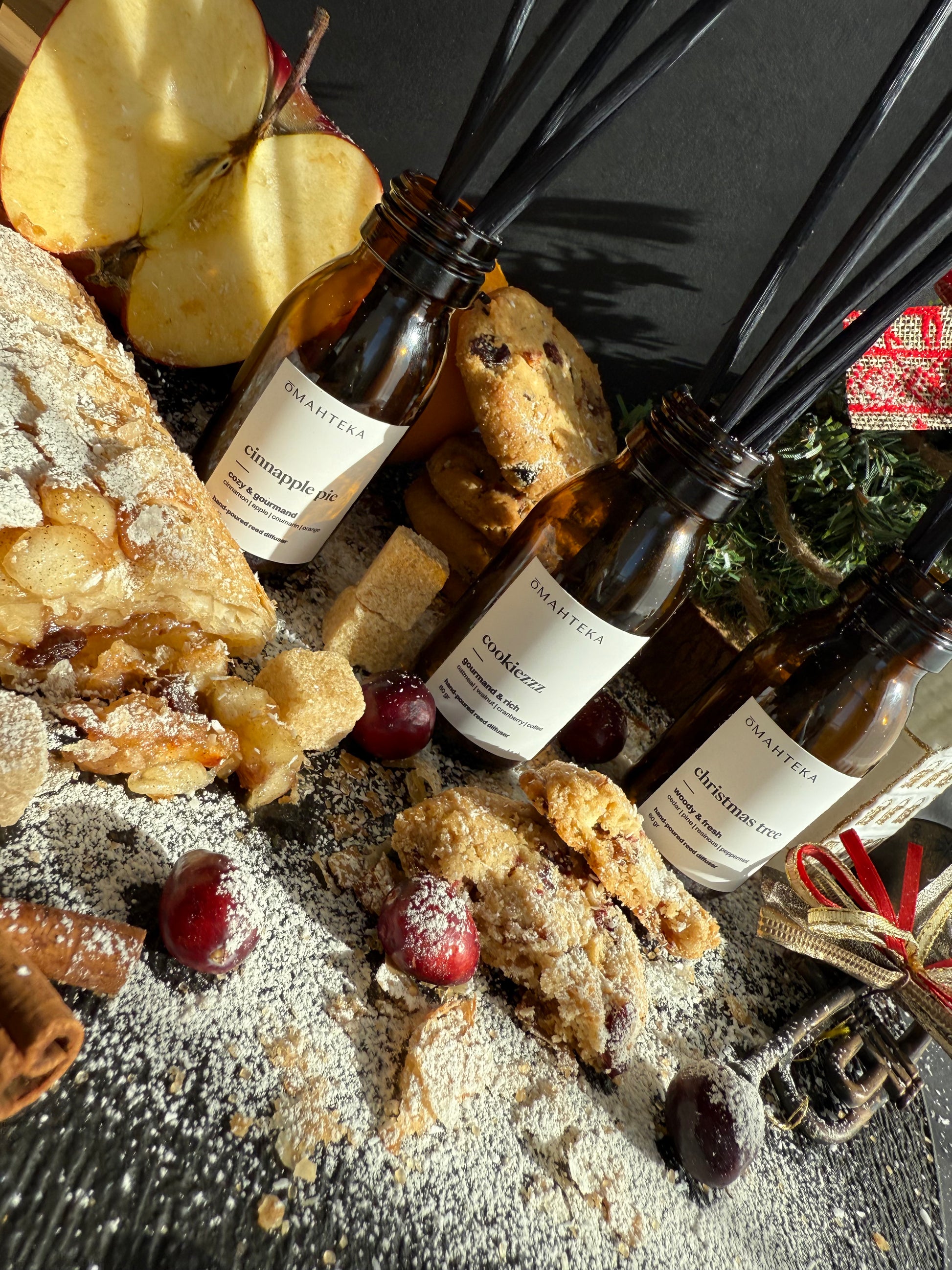 Parfumurile de cameră cu betișoare negre, înconjurate de elemente de iarnă: brad, globuri și texturi cozy.