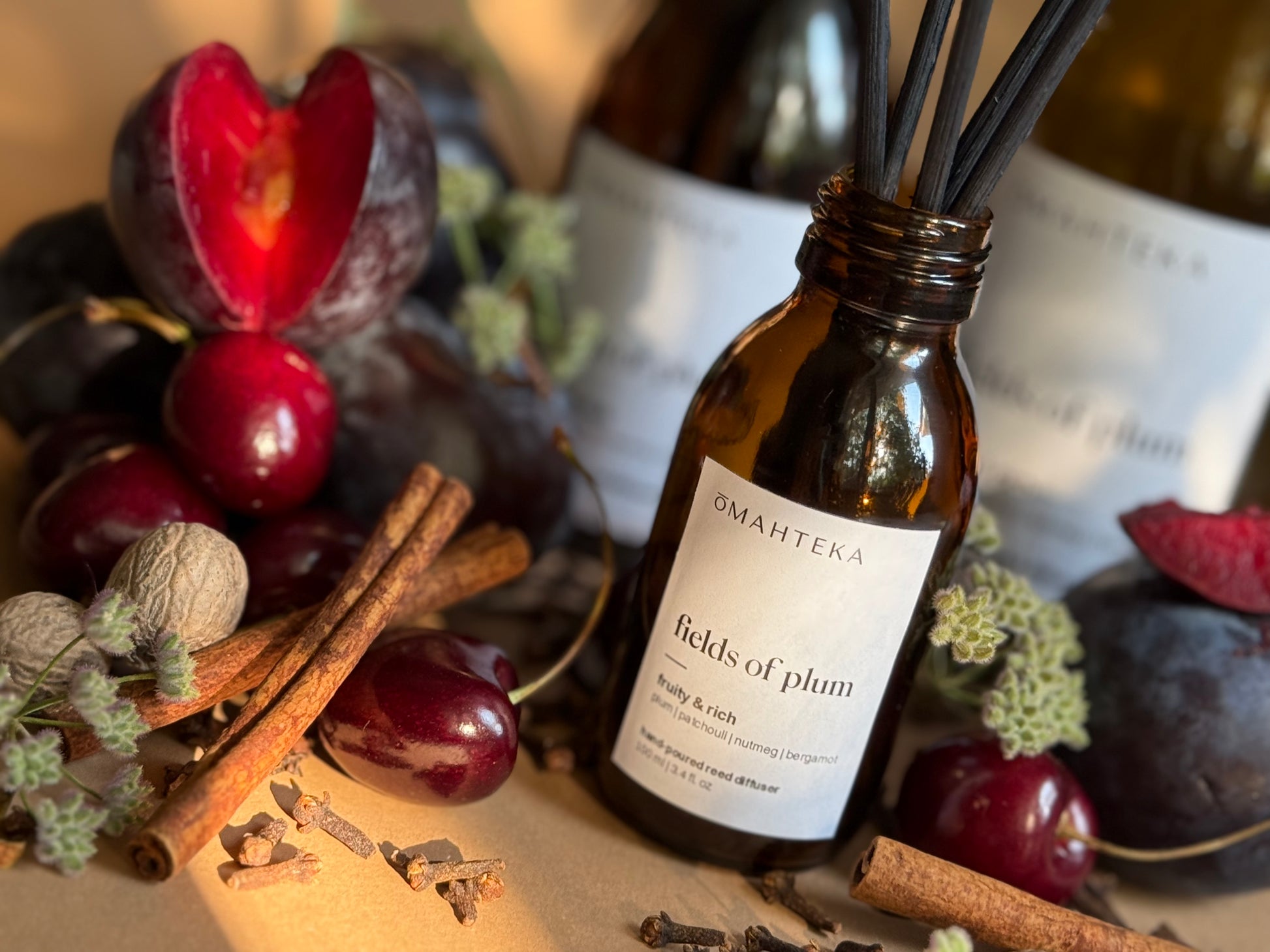 Fields of Plum de la Omahteka – parfum cu bețișoare în sticlă de culoare maro cu protecție UV, în decor cu condimente și cireșe negre.