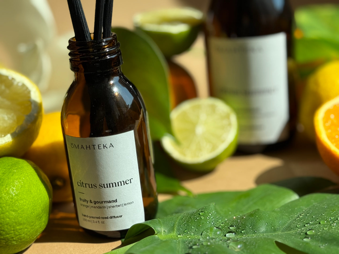 Parfum de cameră Citrus Summer de la Omahteka, cu arome tonice de portocală, lime și frunze verzi, însoțit de bețișoare negre din ratan.