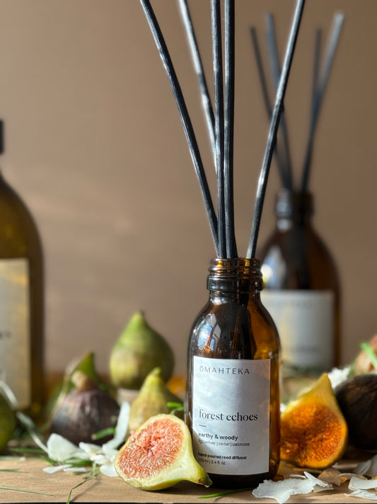 Parfum de cameră Forest Echoes de la Omahteka – difuzor cu bețișoare din ratan și sticlă maro cu protecție UV, în decor natural cu smochine și lemn.