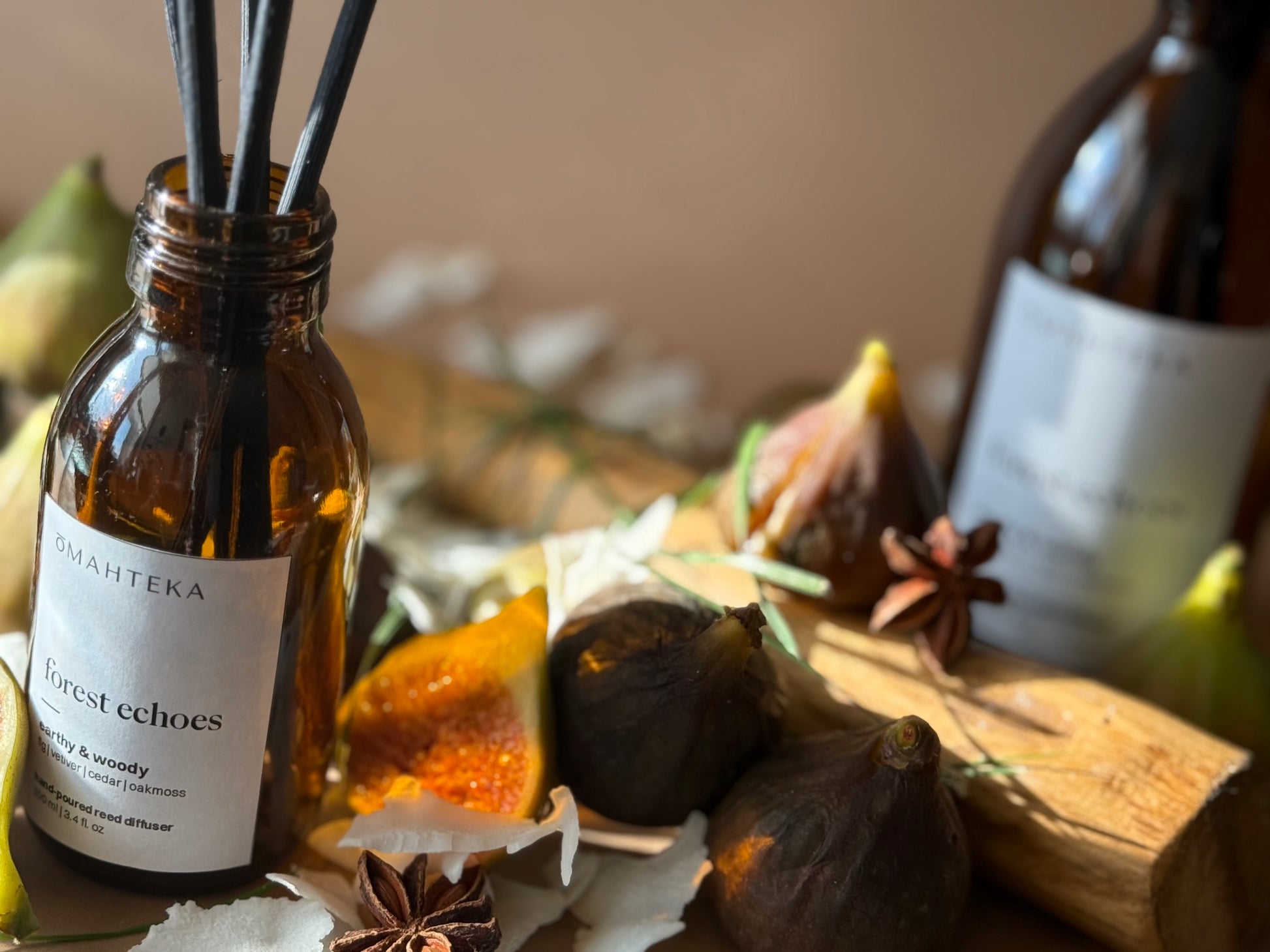 Parfum de cameră Omahteka Forest Echoes, înconjurat de iarbă verde și bucăți de lemn – o esență inspirată din natură, ideală pentru relaxare.